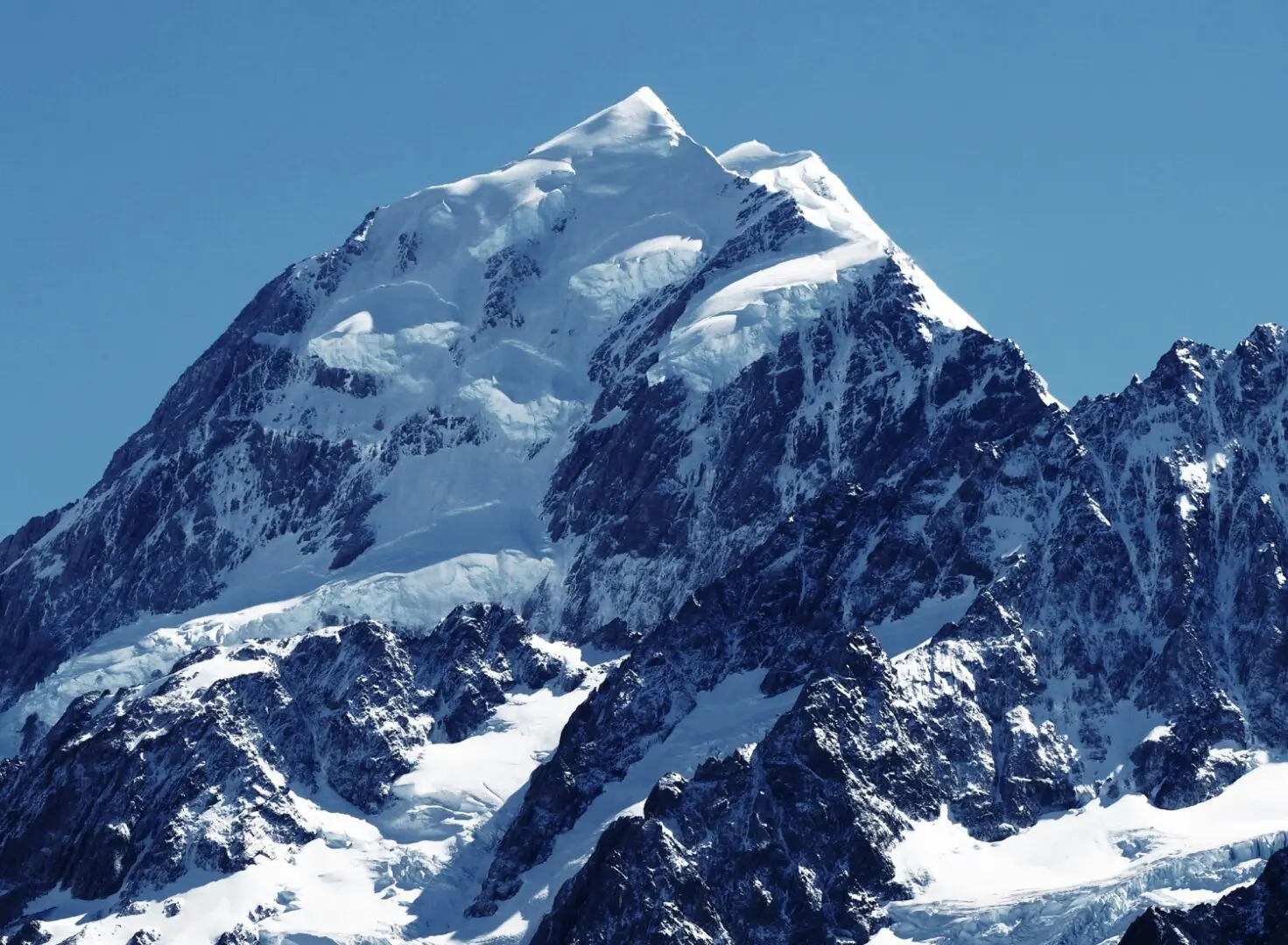 A mountain with snow on it's side and blue sky in the background.